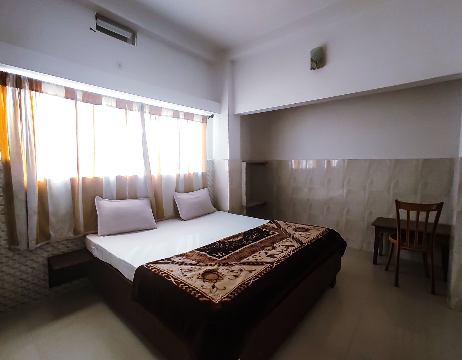 Guest room with double bed and large curtained window at Hotel Vijay, Rajgir