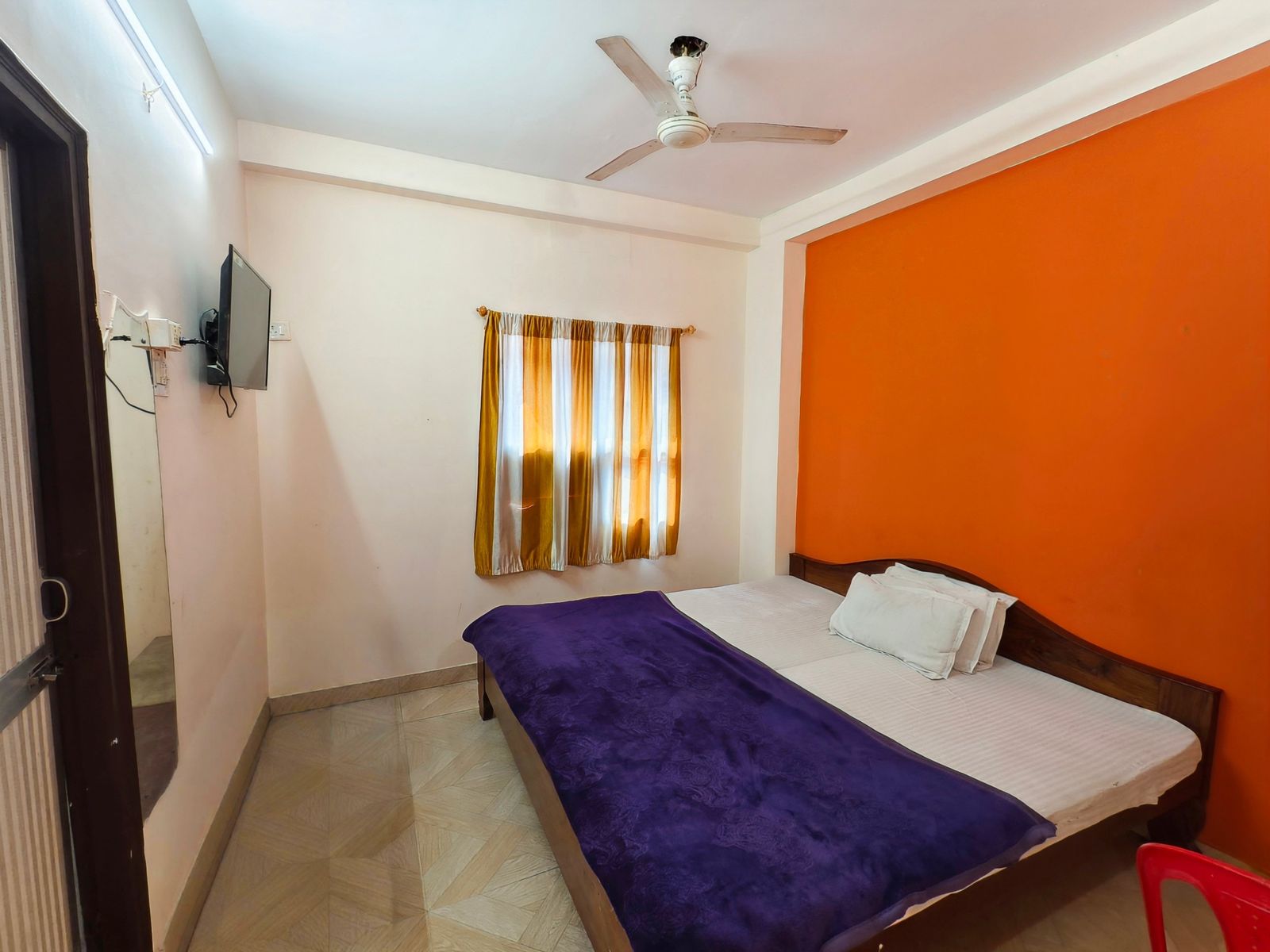 Non-AC room with double bed, orange feature wall and ceiling fan at Hotel Vijay, Rajgir